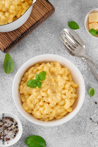 Mac and cheese in a white bowl with fresh basil on top on a gray concrete background. American cuisine, comfort food. Copy space.