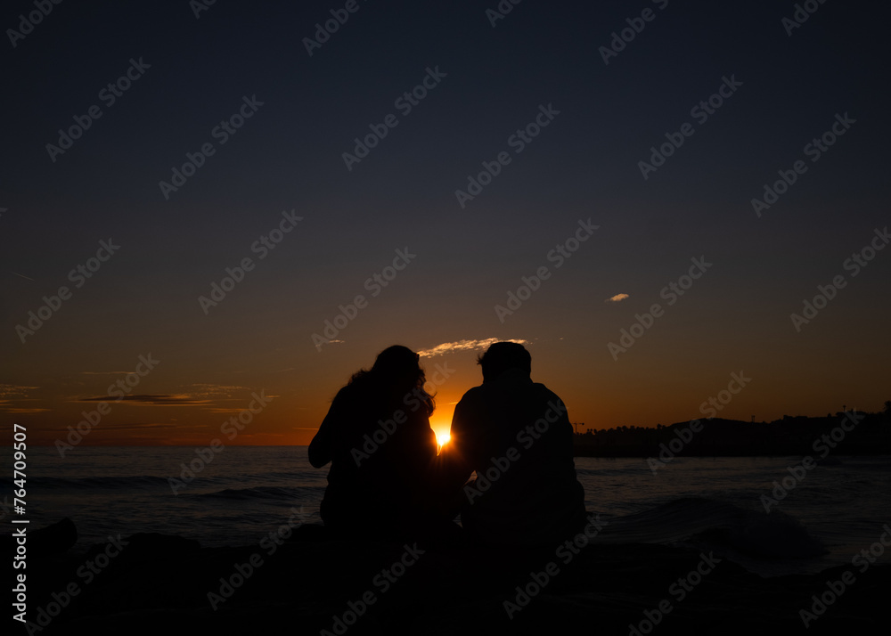 Couple with a sun in between on the seaside at sunset 