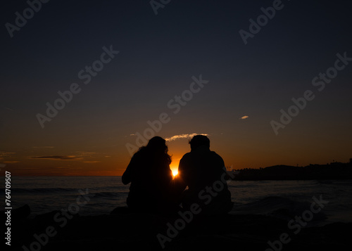 Couple with a sun in between on the seaside at sunset 