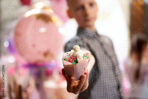 A boy holds a cupcake with mastic in a package in his hand photo