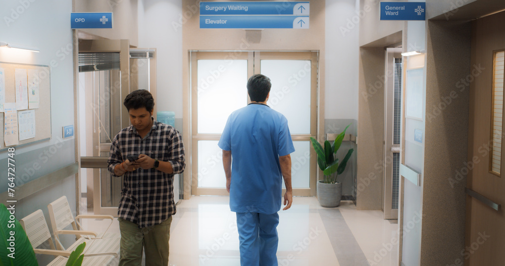 Backview Shot of Young Male Doctor Walking in Hospital Corridor. Indian Professional Medical Specialist Starting his Workday in a Busy Modern Health Clinic