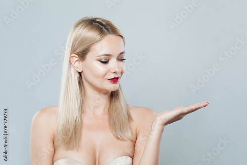 Young blonde lady showing empty open palm hand. Woman with fresh clear skin and long smooth straight hairstile on white background photo