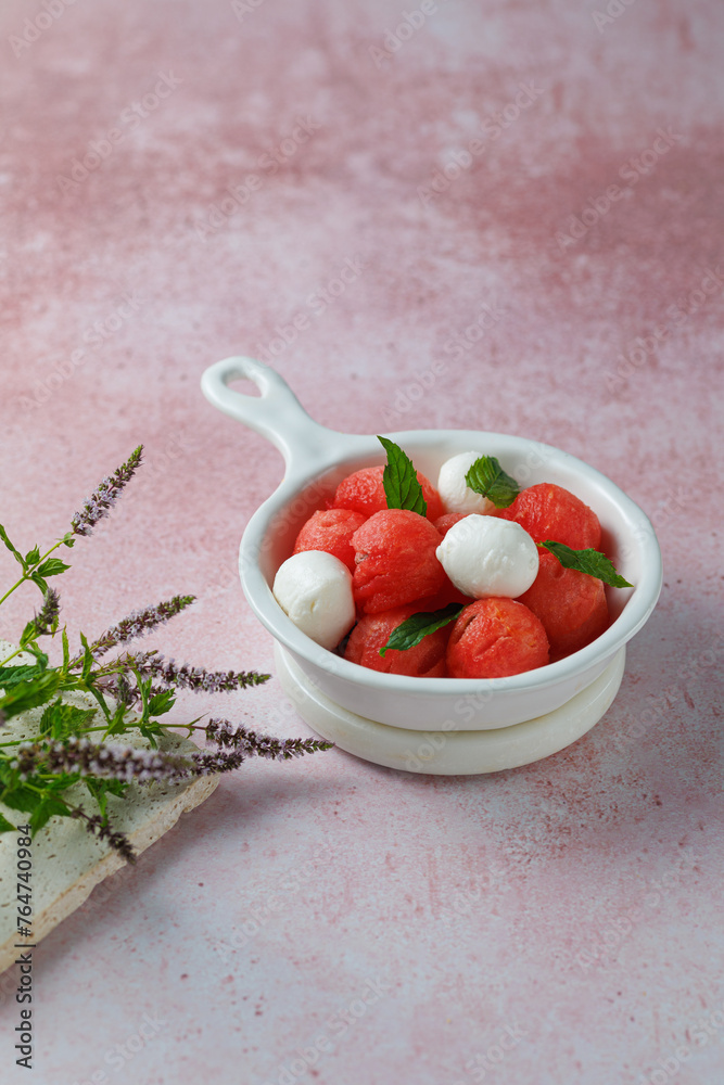 Watermelon Salad with mozzarella balls and mint on light rose background. healthy eating. Summer recipe concept Watermelon Salad with mozzarella balls and mint on light rose background. healthy eating. Summer recipe concept