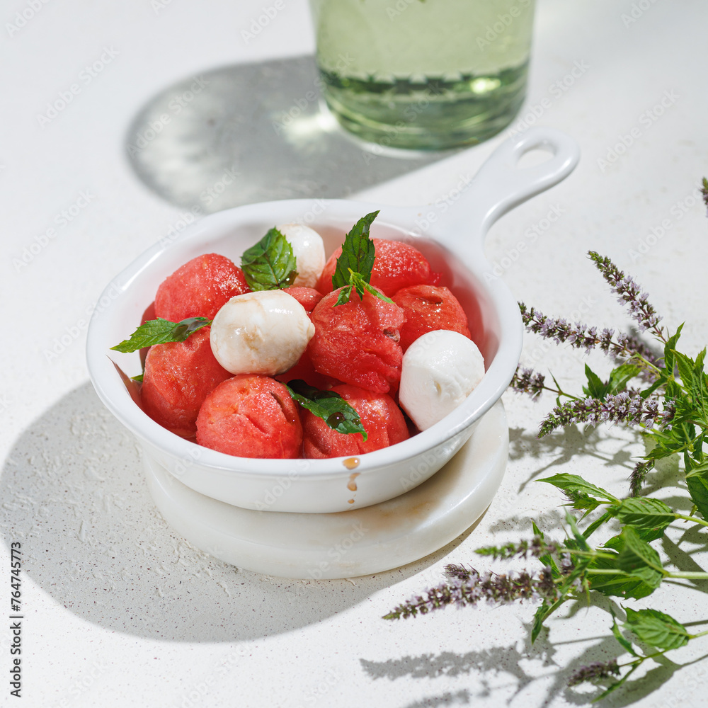 Fruit salad with watermelon balls and mozzarella cheese in white ceramic bowl on light white background Fruit salad with watermelon balls and mozzarella cheese in white ceramic bowl on light white background