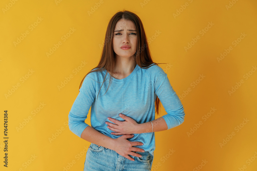 Having stomach pain. Young woman is against yellow background Having stomach pain. Young woman is against yellow background