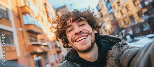 A cheerful man with curly hair is smiling and expressing happiness while standing on a lively urban street