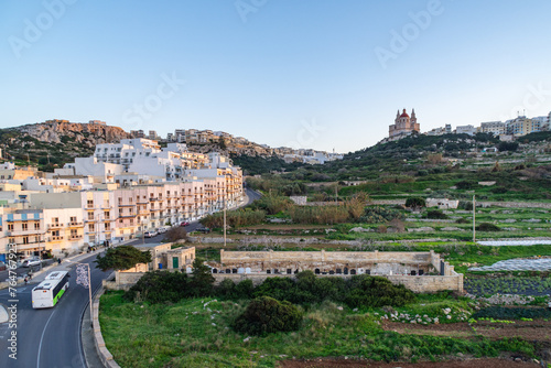 Triq Il-Marfa, Mellieha, Malta - December 25th 2022: A bus passing the small Mother of Mercy Cemetery overlooked by the parish church.