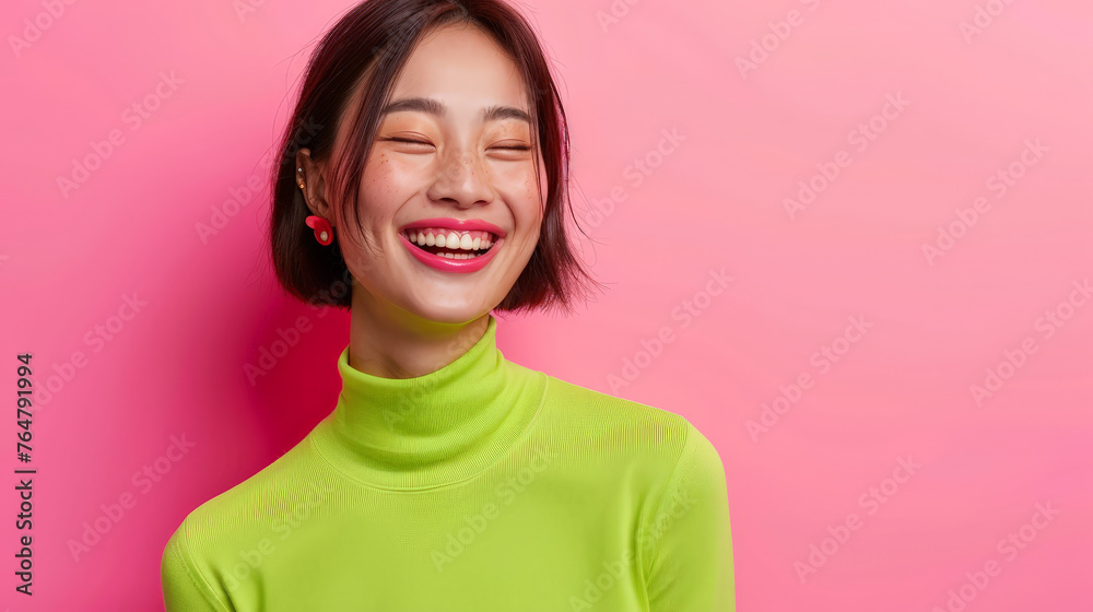 Exuberant Joy: Asian Woman Laughing with Eye-Catching Green Top on Pink Background Exuberant Joy: Asian Woman Laughing with Eye-Catching Green Top on Pink Background