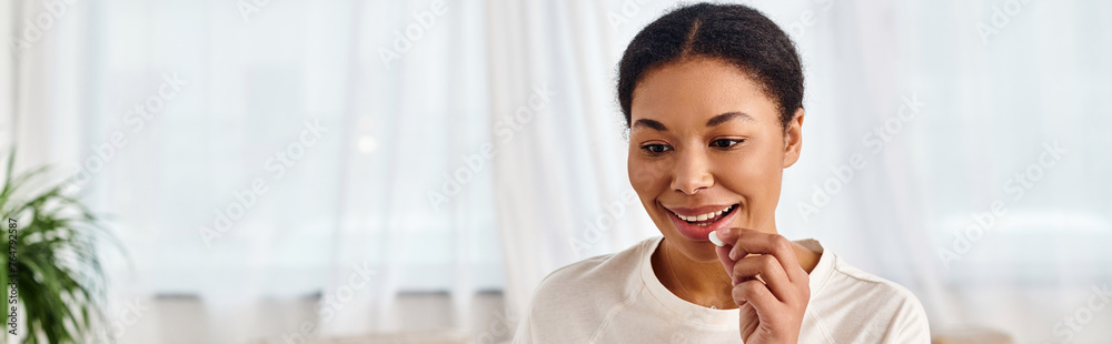 banner of happy african american woman taking pill at home, perfect for health and wellness banner of happy african american woman taking pill at home, perfect for health and wellness
