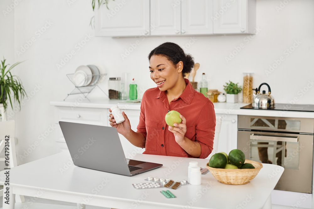 african american nutritionist holding apple and supplements while offering health advice online