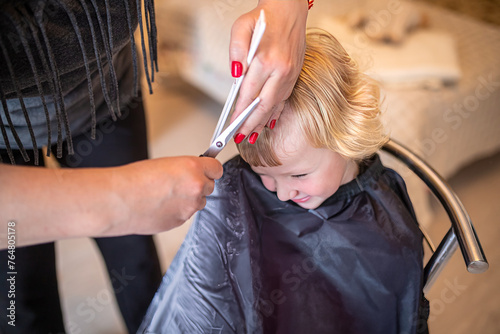A beautiful little lady does a hairstyle. A professional stylist cuts bangs for a child at home in a home interior. Children's Hairdress