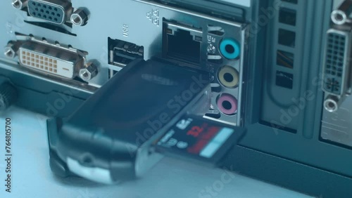 A man's hand inserts and removes a SD card reader into the USB port on the back panel of the computer. Closeup. Macro photo