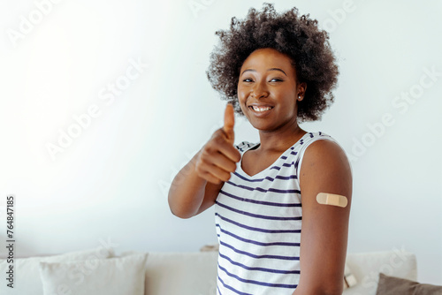 Young african american woman showing thumb up and her arm with band aid after coronavirus Covid-19 vaccine injection. Covid vaccination concept.