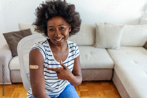 Portrait of a young African American woman wearing a bandaid after getting vaccinated. Smiling black woman looking positive about getting the vaccine and posing against a bright background. photo