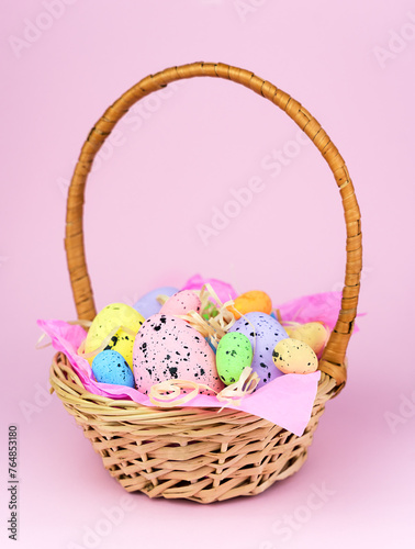Decorative Easter Eggs in a wicker basket on a pink background. Easter decor. Selective focus.