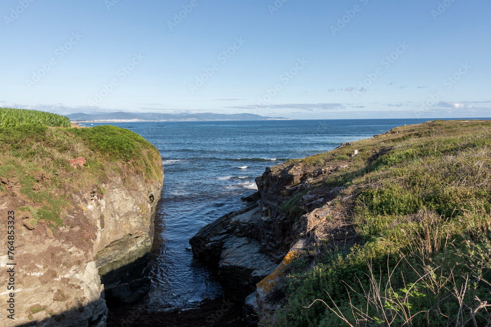 A serene coastal scene with grassy cliffs, rocky shores, and a calm sea under a clear sky, evoking tranquility