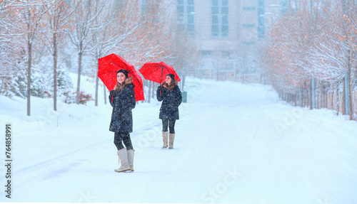 Beautiful girl in black coat with red umbrella walking down the road while snowfall
