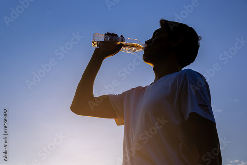 Silhouette of young man runner with a bottle of water freshness after training outdoor workout.	