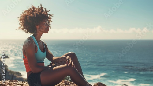 afro woman with sporting clothes is sitting near the ocean in a natural environment 