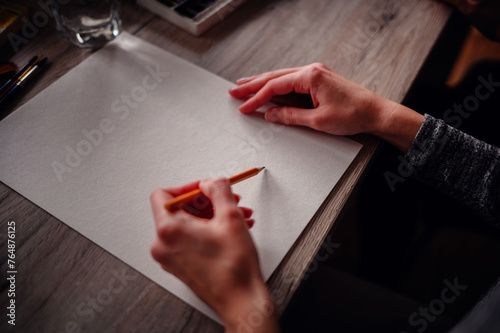 Close-up of hands holding a pencil poised to start a drawing, highlighting the potential of a blank page
