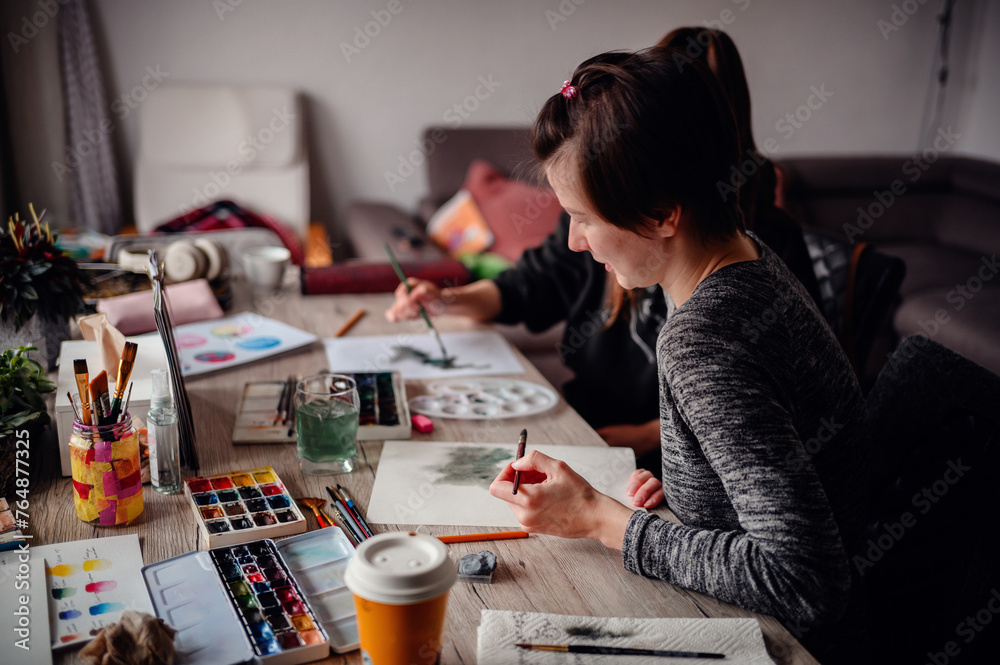 Two individuals engage in painting at home, immersed in a cozy artistic collaboration with brushes and watercolors