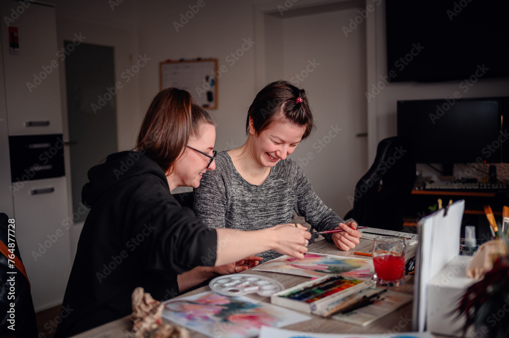Fototapeta premium Two artists share a moment of creation, painting with watercolors in a home setting, showcasing teamwork and artistic expression