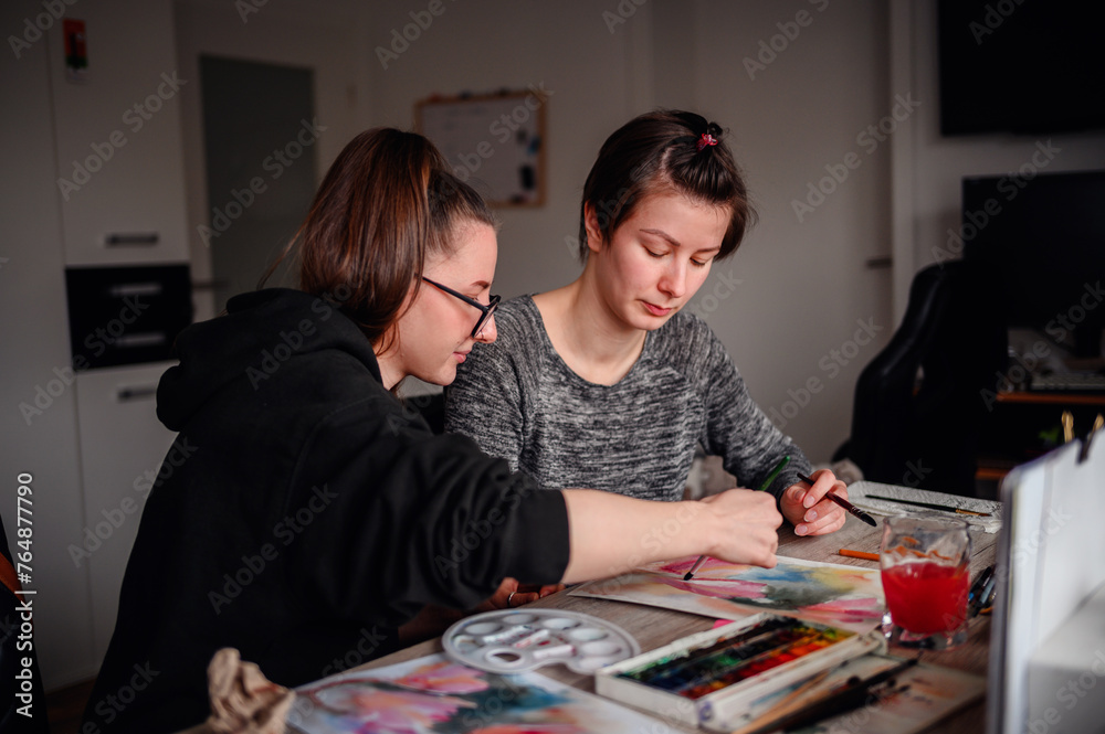 Two artists share a moment of creation, painting with watercolors in a home setting, showcasing teamwork and artistic expression