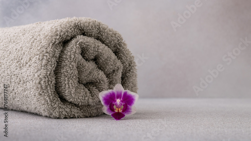 Fotografi Luxurious grey towel neatly rolled and placed beside a vibrant purple orchid flo