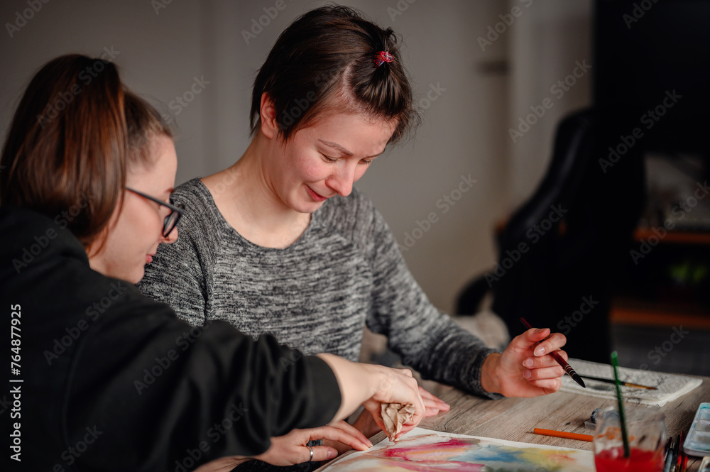 Fototapeta premium Two friends share laughter and joy while engaged in watercolor painting, illustrating the pleasure of artistic hobbies.