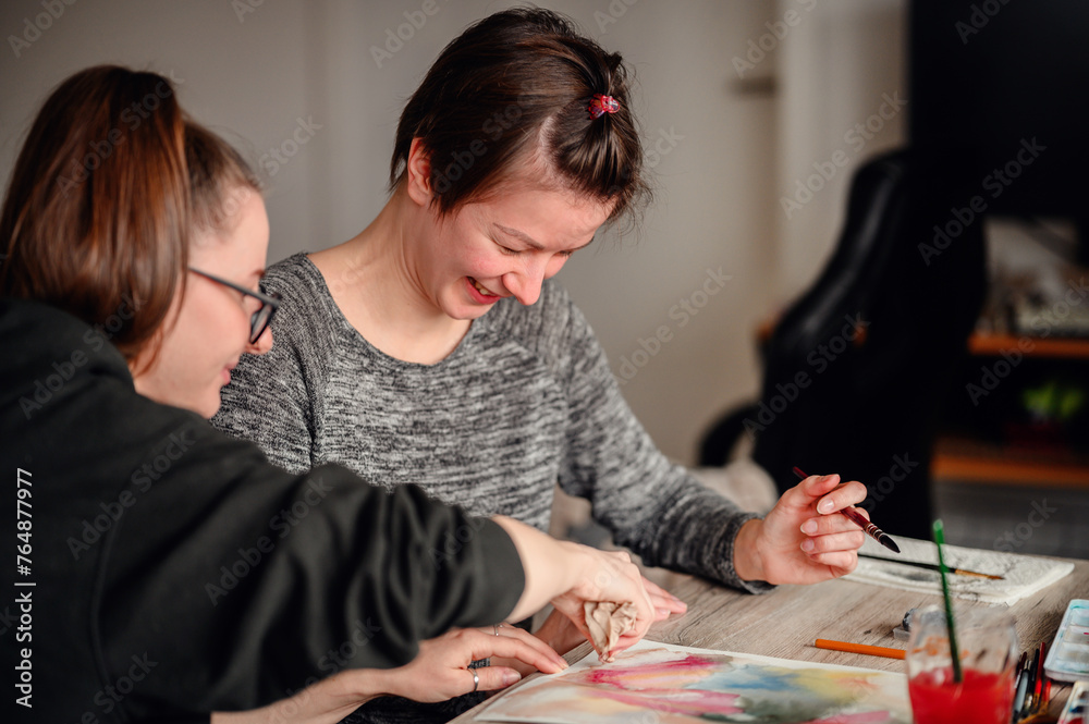 Fototapeta premium Two friends share laughter and joy while engaged in watercolor painting, illustrating the pleasure of artistic hobbies.