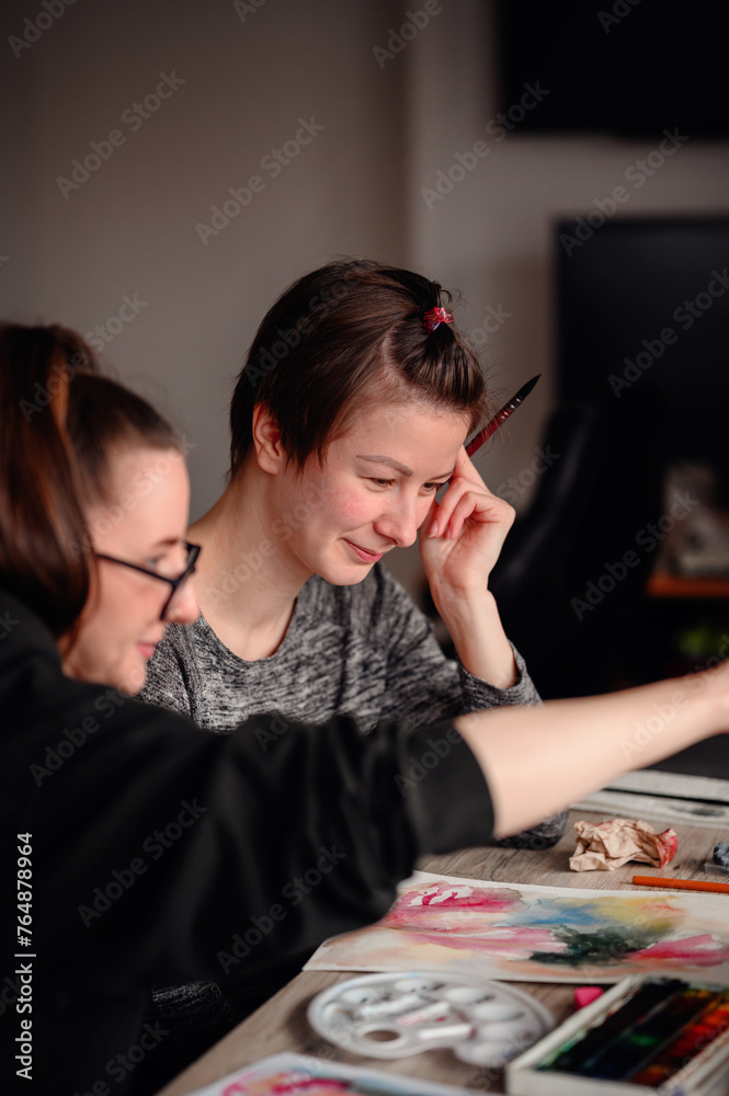 Two friends share laughter and joy while engaged in watercolor painting, illustrating the pleasure of artistic hobbies.