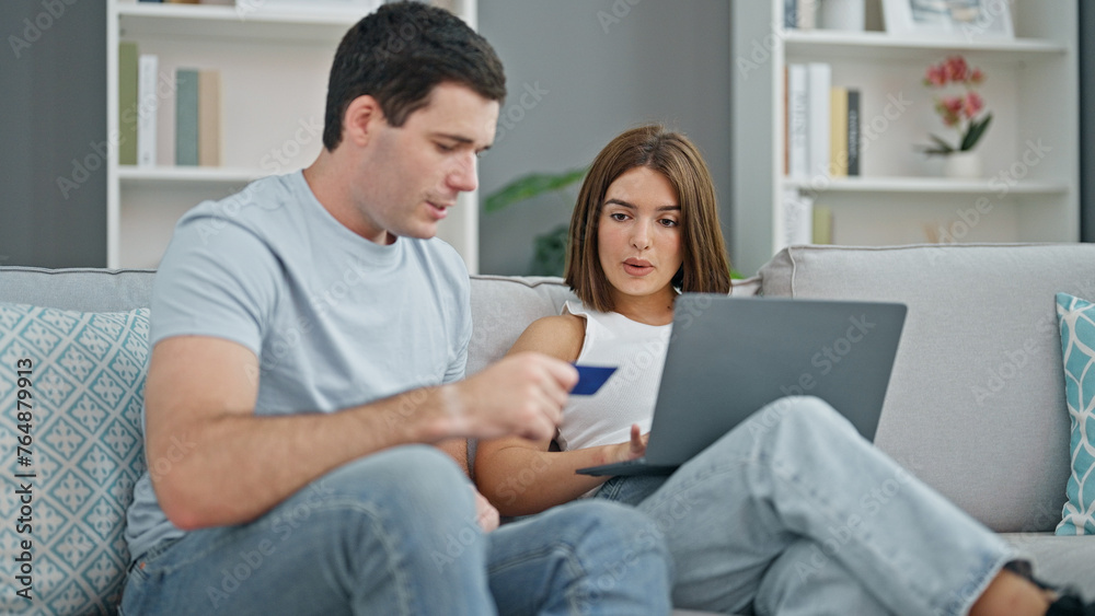 Beautiful couple shopping with laptop and credit card sitting on sofa at home