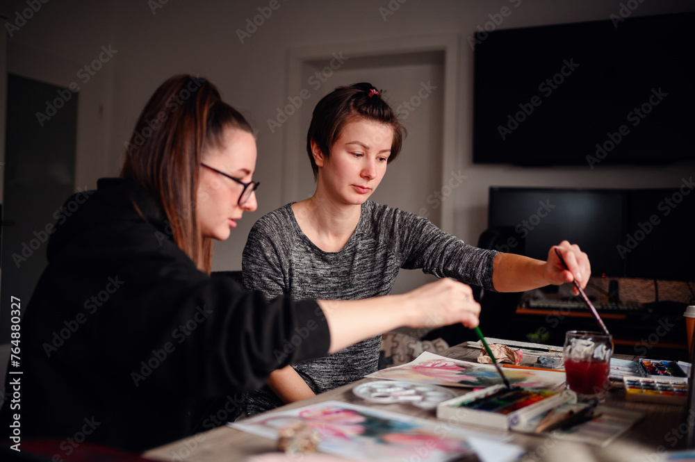 Two artists deeply focused on their watercolor techniques, a synergy of concentration and creativity fills the room