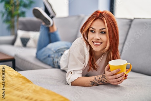 Young caucasian woman drinking coffee lying on sofa at home