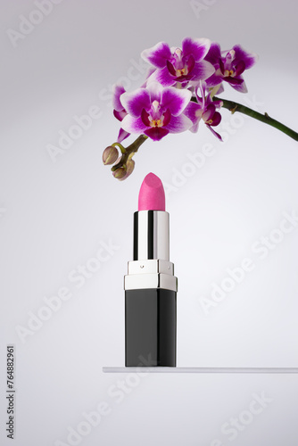 An elegant vibrant pink lipstick beside a beautiful purple orchid flower