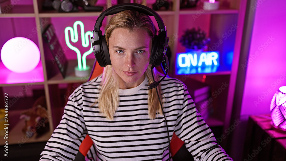 A beautiful young woman wears headphones in a vibrant home gaming room adorned with neon lights.