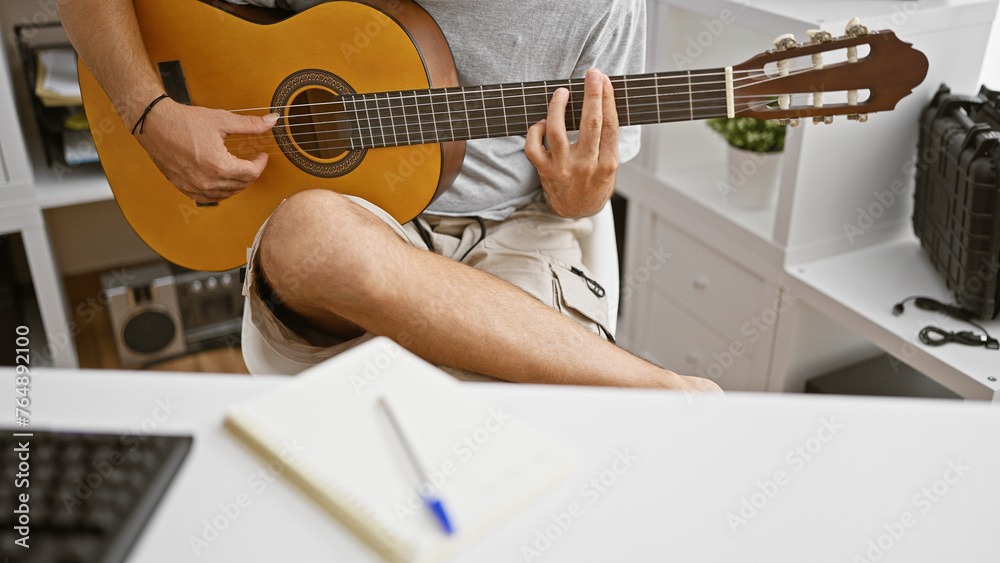 Fototapeta premium Young hispanic man playing an acoustic guitar indoors, showcasing musical talent and creativity.