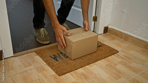 A young man picking up a cardboard box from a welcome mat in a home interior, showcasing a casual lifestyle moment.