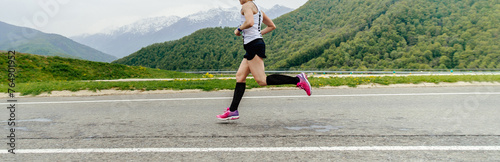 female athlete in black compression socks running road in background mountains and forests photo