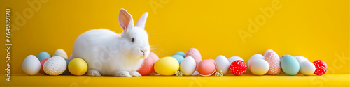 White rabbit and multi-colored Easter eggs on the yellow background.
