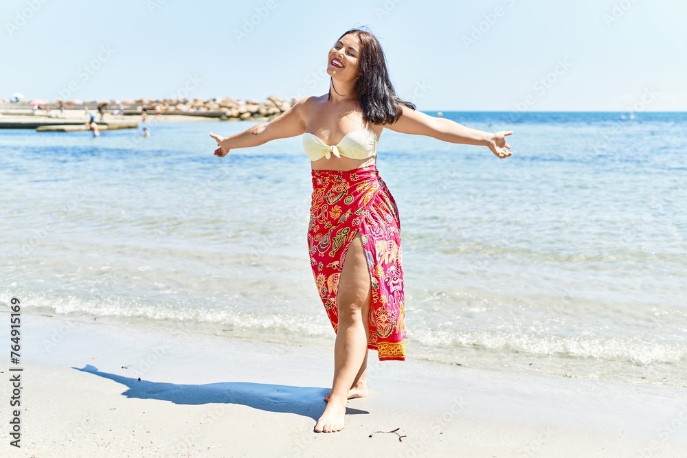 Young beautiful hispanic woman tourist wearing bikini with arms open at seaside Young beautiful hispanic woman tourist wearing bikini with arms open at seaside