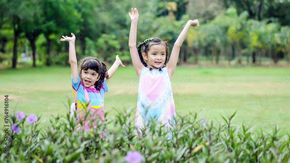 Happy two young girls raising hands together in park, Cute Little Girl having fun, Exuberant little child enjoying spring season in the park. Happy two young girls raising hands together in park, Cute Little Girl having fun, Exuberant little child enjoying spring season in the park.