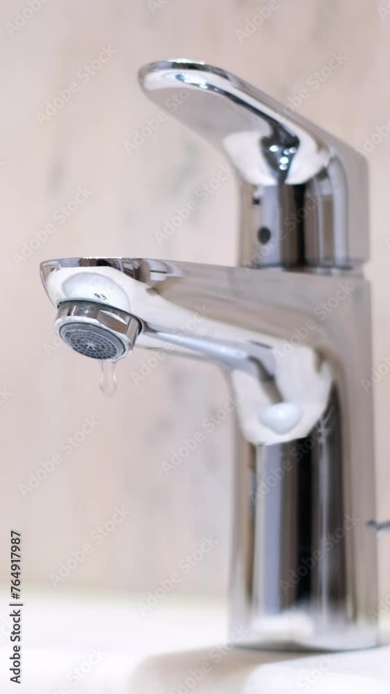 Drop of water drips from the tap. Beautiful fresh and clean water flowing from a tap. Close-up front view slow motion broken chrome faucet in the bathroom. Everyday problems, wasting water and energy. Drop of water drips from the tap. Beautiful fresh and clean water flowing from a tap. Close-up front view slow motion broken chrome faucet in the bathroom. Everyday problems, wasting water and energy.