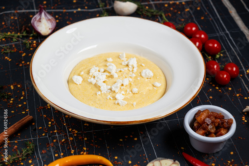 Banush or banosh is a Ukrainian dish prepared from cornmeal with cream topped with bacon, onion and bryndza closeup on the bowl on the wooden table. Vertical top view from above photo