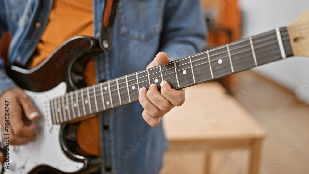 Close-up of a man playing guitar indoors, focusing on hand and strings for a musical concept.