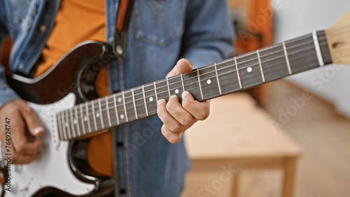 Close-up of a man playing guitar indoors, focusing on hand and strings for a musical concept.