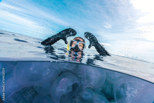 A woman in a black wetsuit is in the water with jellyfish split shot