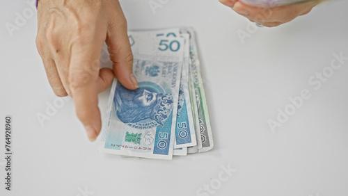 Фотография A mature woman counts polish zloty banknotes against a white background, indicating finance management and savings