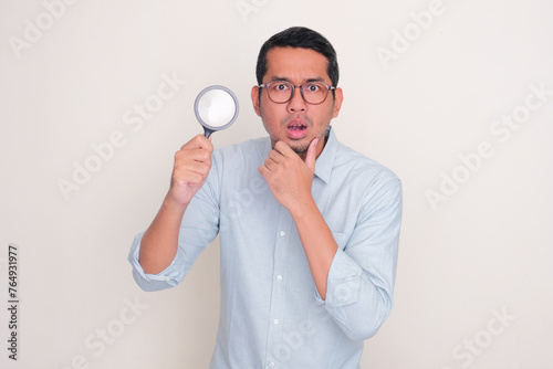 Adult man looking camera with suspicious expression while holding magnifying glass photo