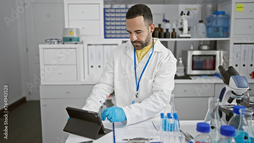 Hispanic man in lab coat using tablet in laboratory setting with equipment and microscope